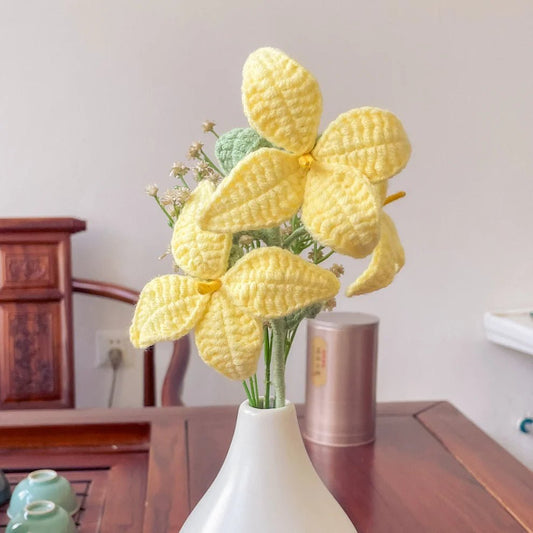 Crocheted yellow butterfly flowers in white vase on wooden surface