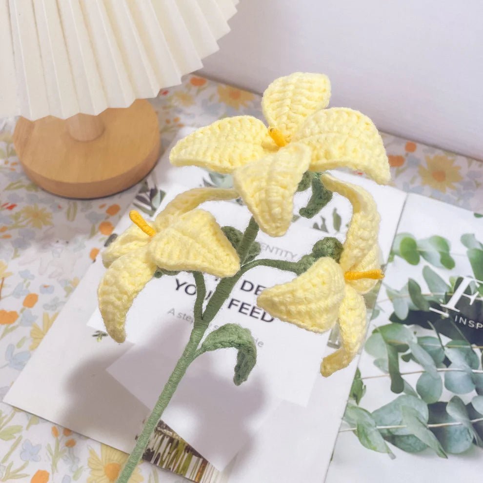 Crocheted yellow lily with green stem on floral patterned background near wooden lamp