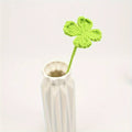 Bright green crocheted four-leaf clover in a minimalist white ceramic vase