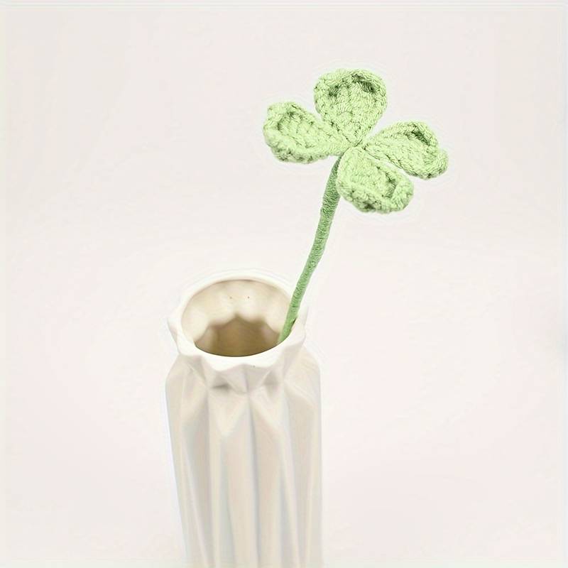 Knitted four-leaf clover in white ceramic vase against soft background