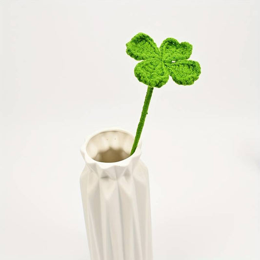 Crocheted green four-leaf clover sitting in a white textured ceramic vase