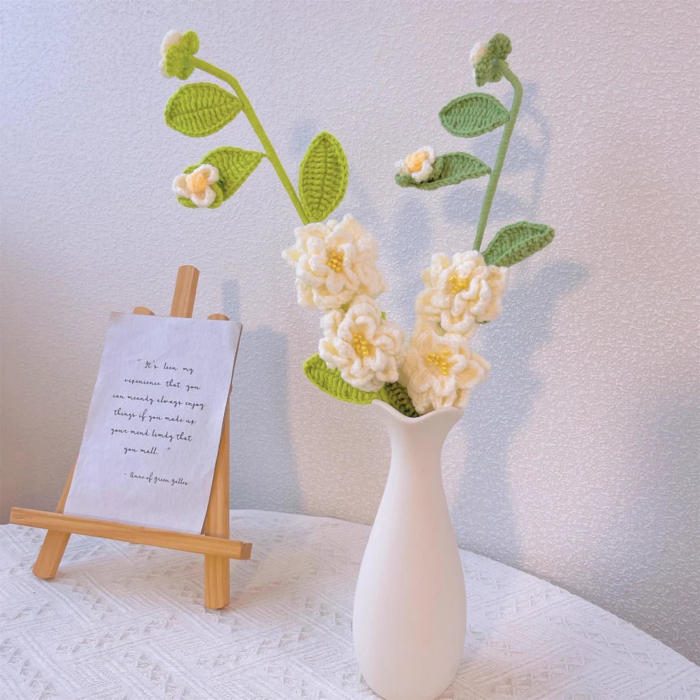 Crocheted white flowers in ceramic vase with handwritten note on wooden stand