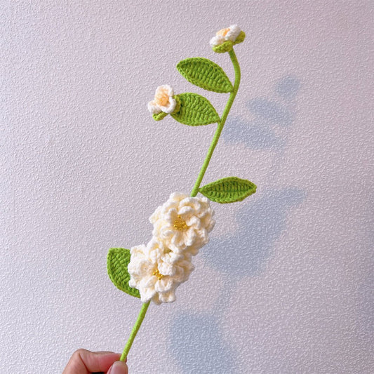 Crocheted white flower with green leaves on delicate stem, held by a hand