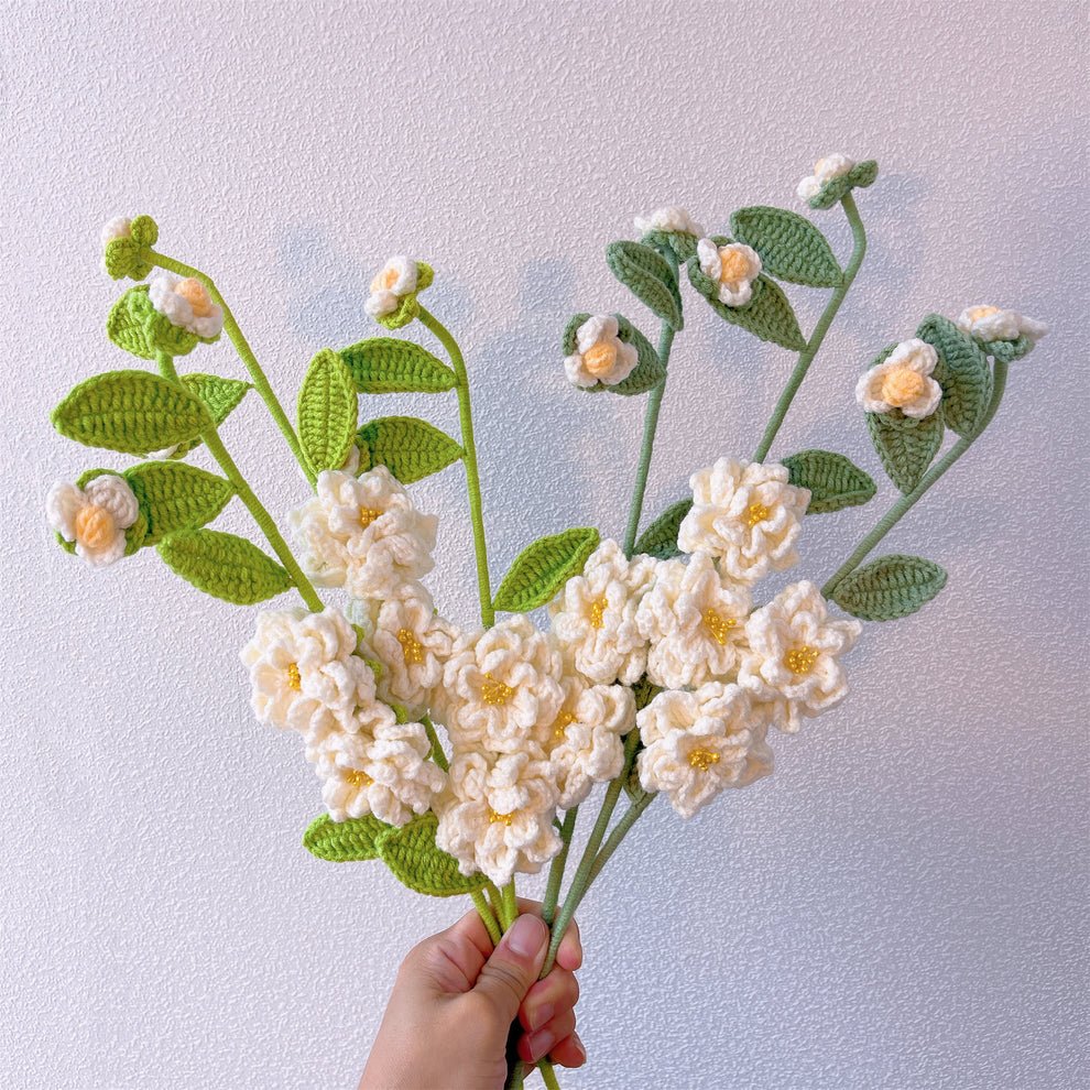 Crocheted white flowers with yellow centers and green leaves held in a hand