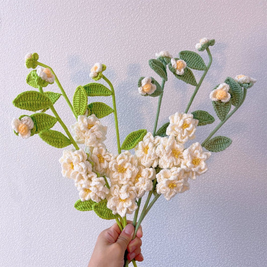 Crocheted white flowers with yellow centers and green leaves held in a hand