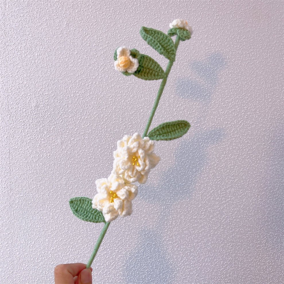 Crocheted white flowers with green leaves on a delicate stem, held by a hand