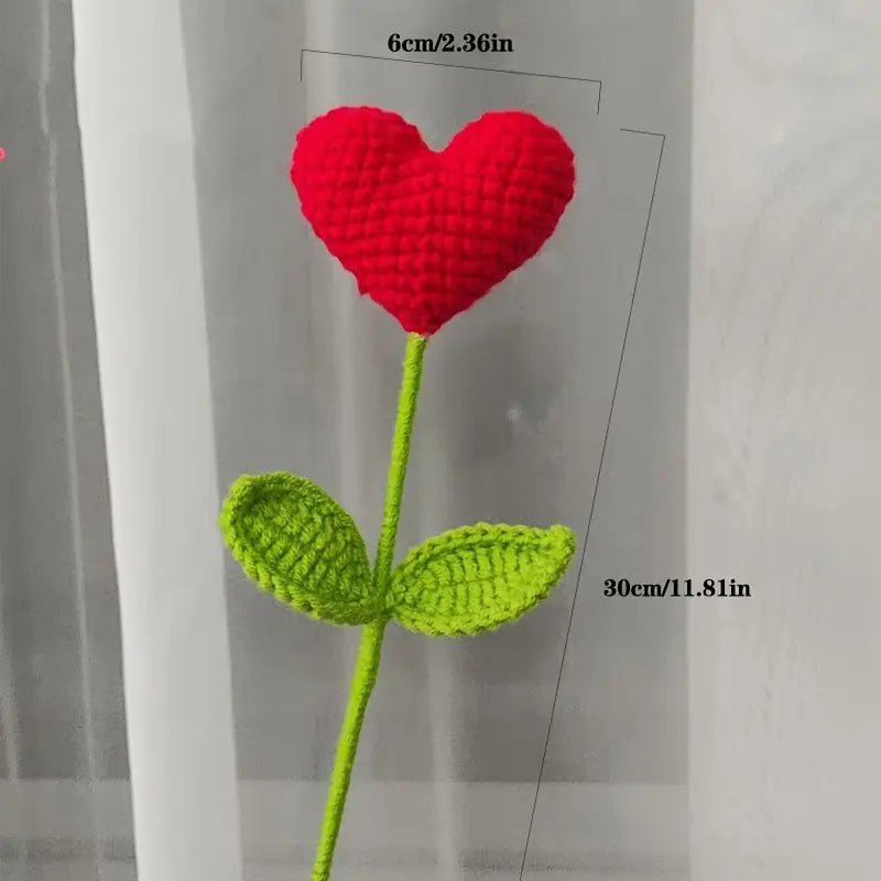 Crocheted red heart flower with green stem and leaves against gray background
