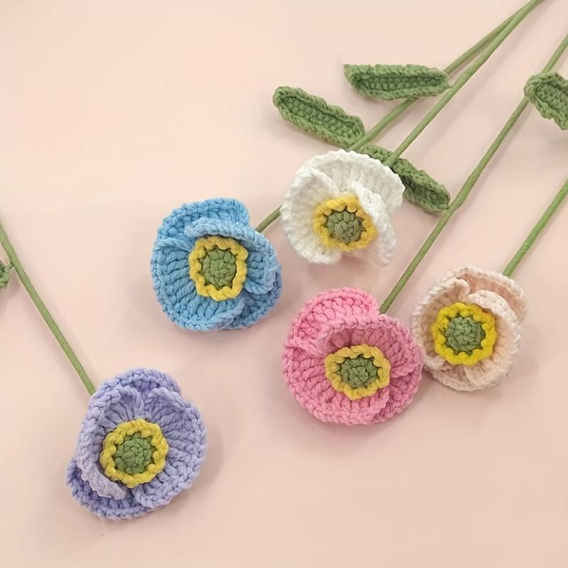 Crocheted flowers in blue, pink, purple, and white with green stems on pastel background