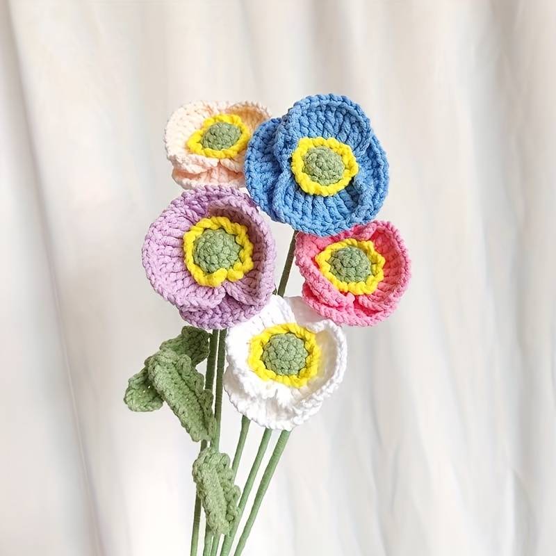 Crocheted colorful flowers with yellow centers, green stems on soft background