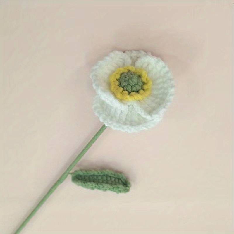 Crocheted white flower with yellow center and green stem on pale background