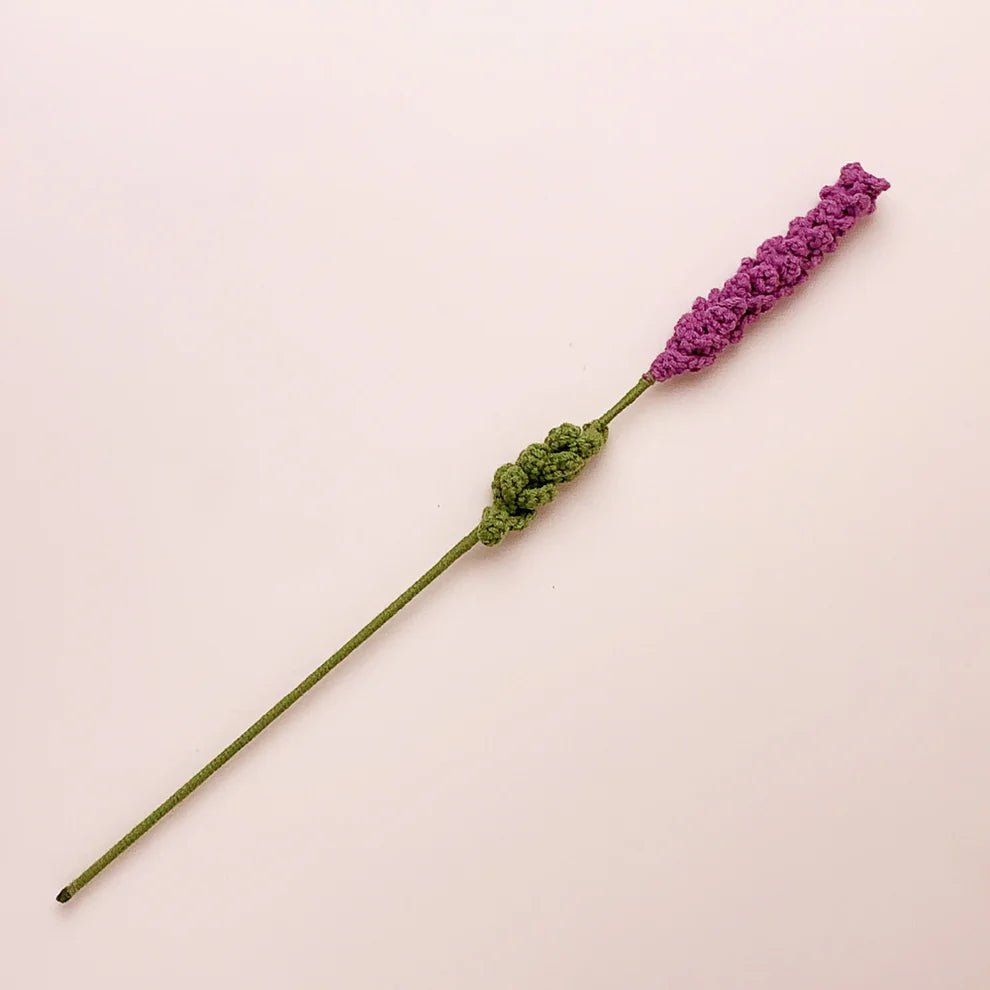 Crocheted lavender stem with purple flower and green leafy base on pale background