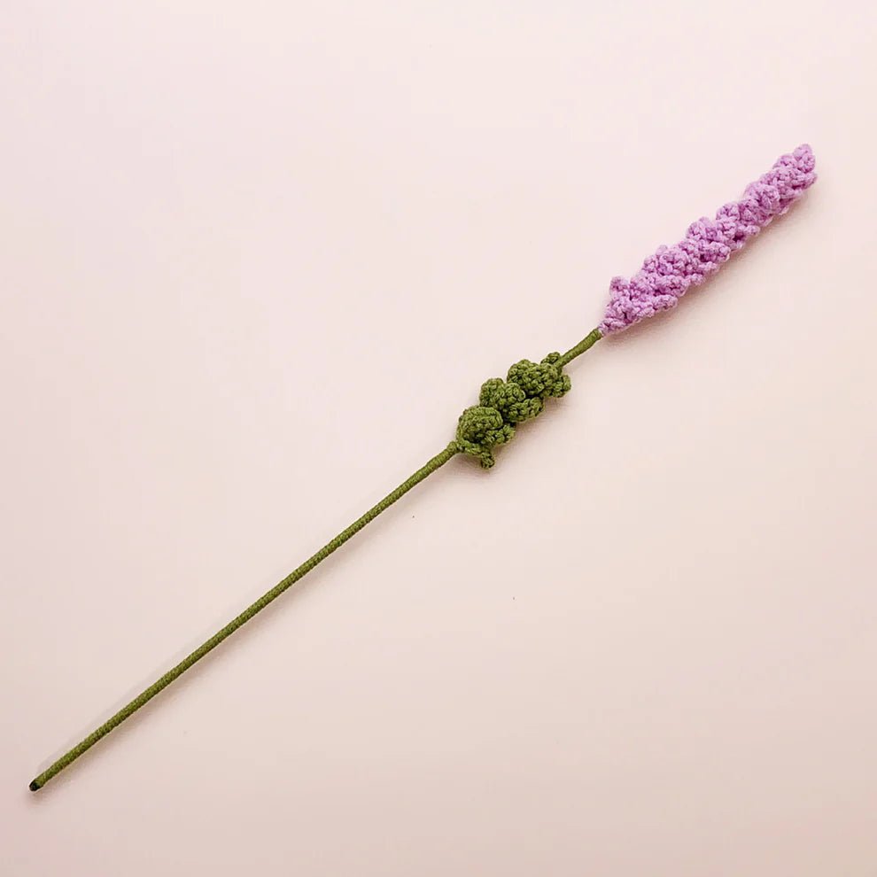 Crocheted lavender flower with green stem on light pink background