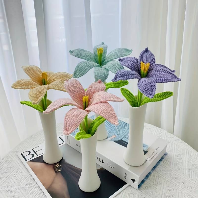Crocheted lily flowers in pastel colors displayed in white vases on books near curtained window