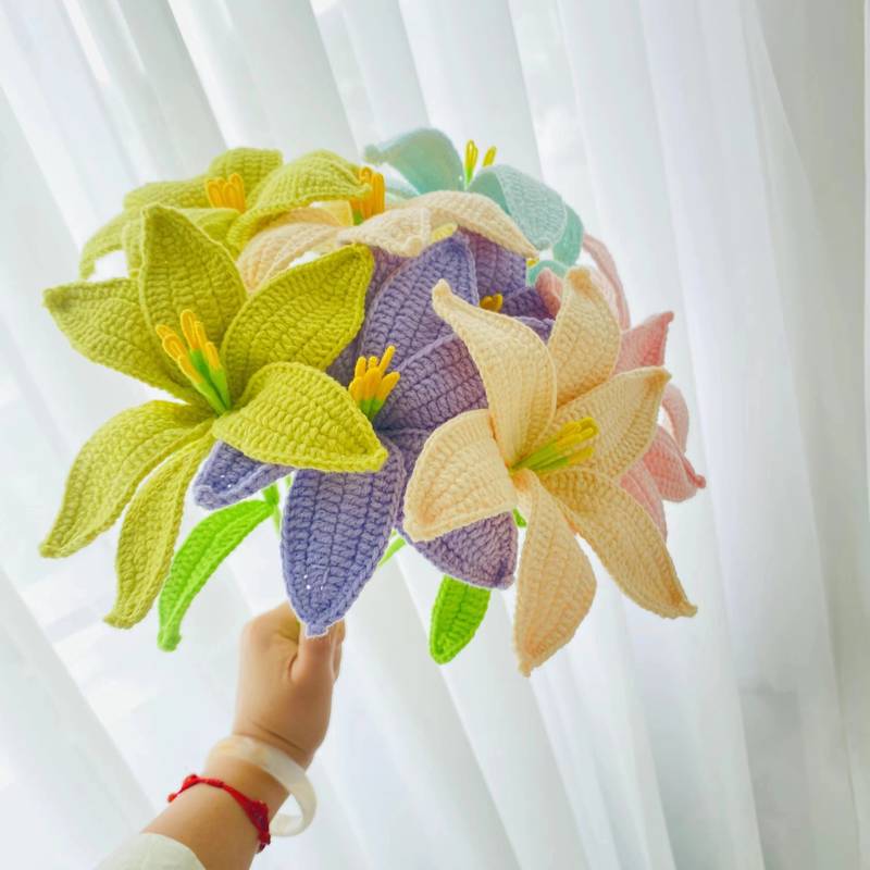 Crocheted colorful lilies in green, purple, yellow, and pink held by a hand