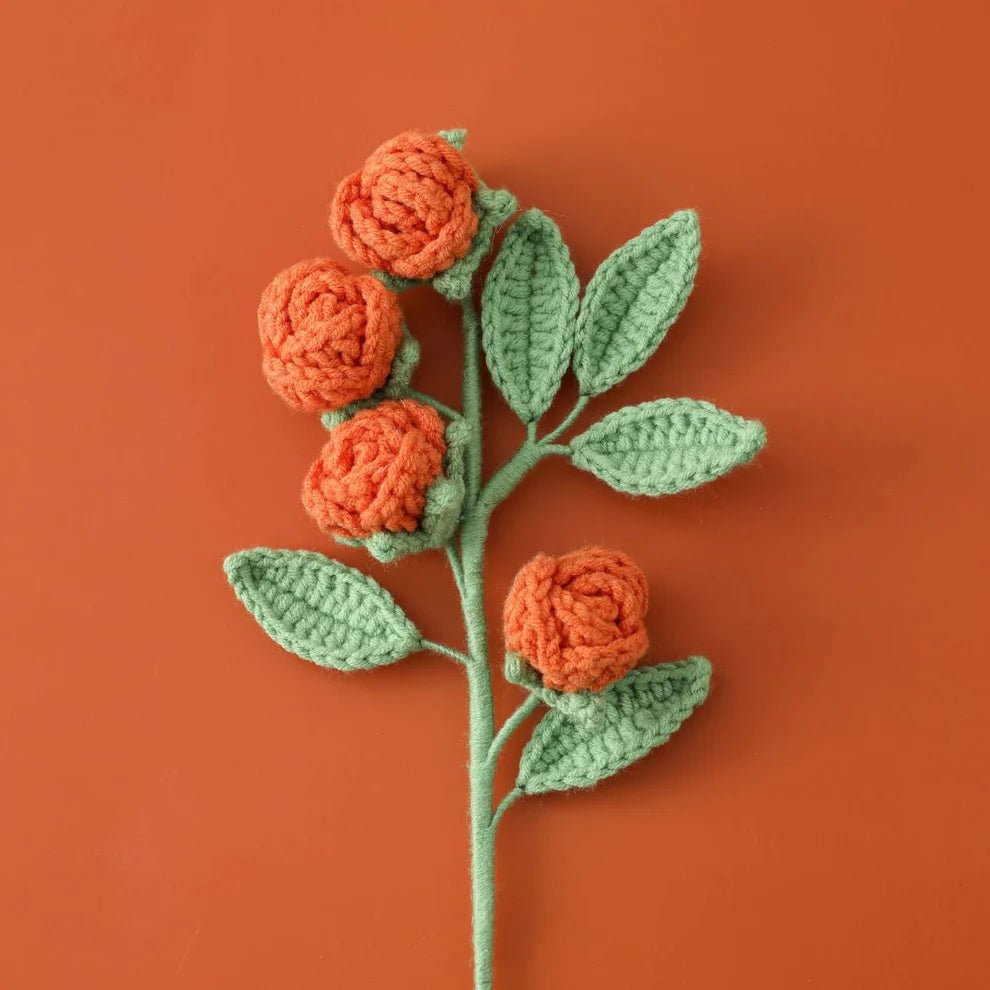 Crocheted orange roses with green leaves on an orange background