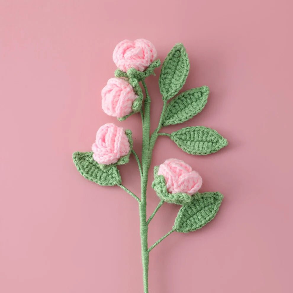 Crocheted pink roses with green leaves on a soft pink background