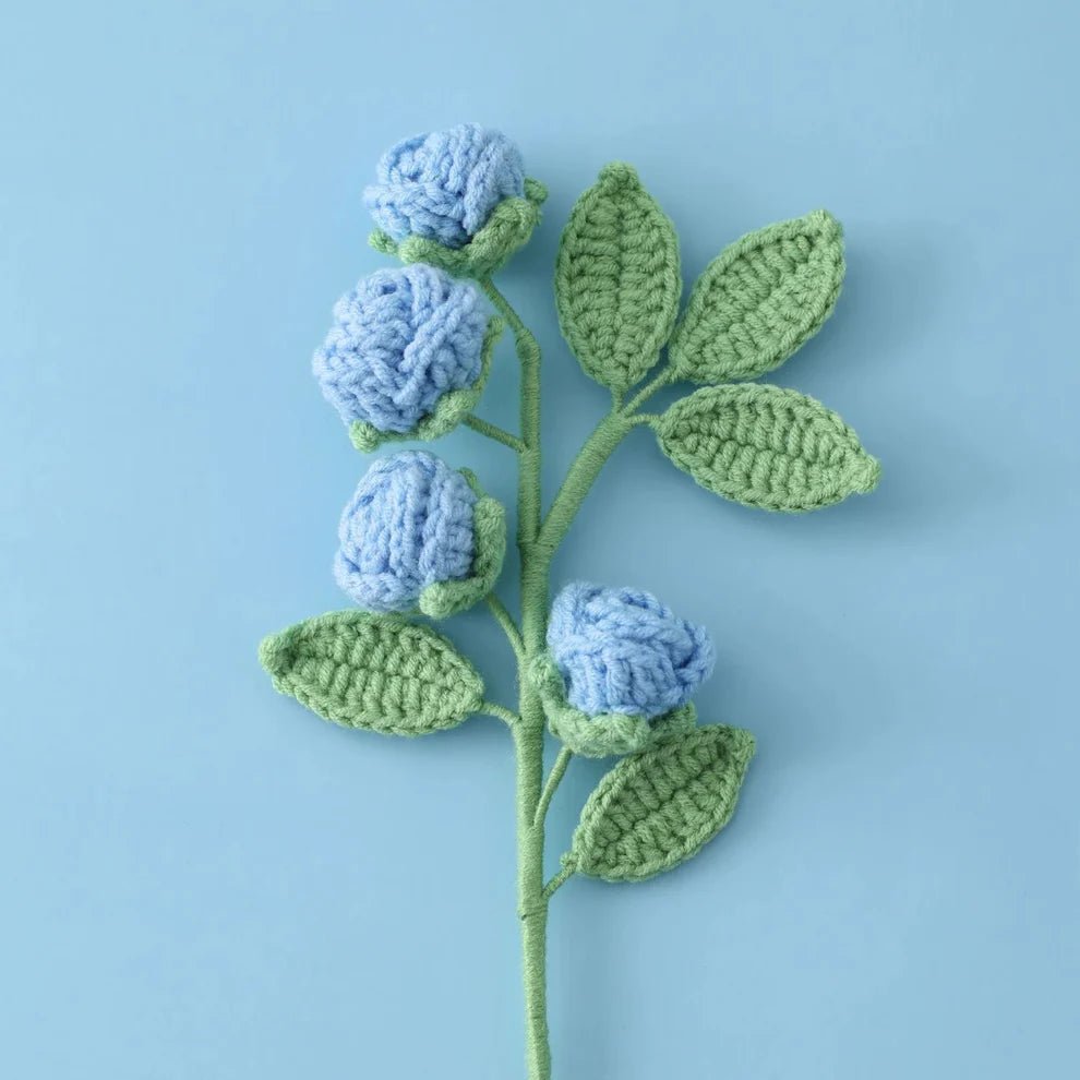 Crocheted blue flowers and green leaves on a light blue background
