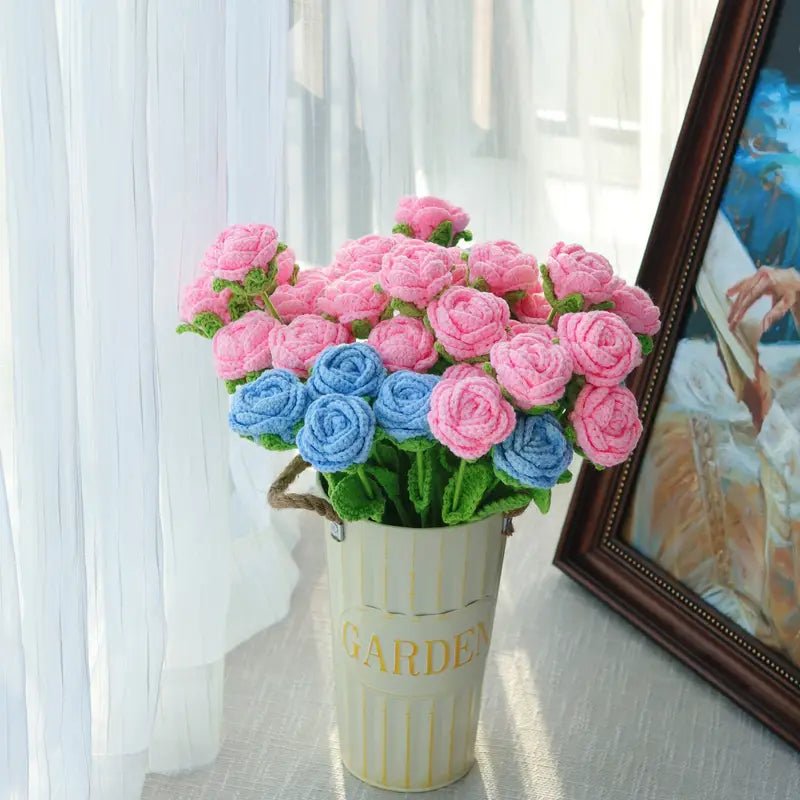 Crocheted pink and blue roses in a white "Garden" vase by a curtained window