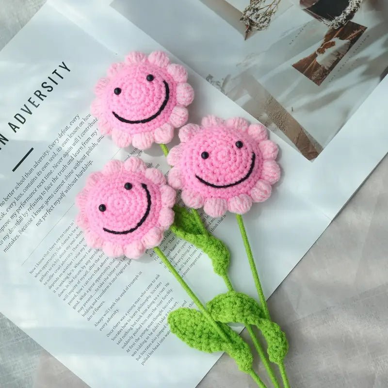 Three pink crocheted smiley face flowers with green stems on a text background