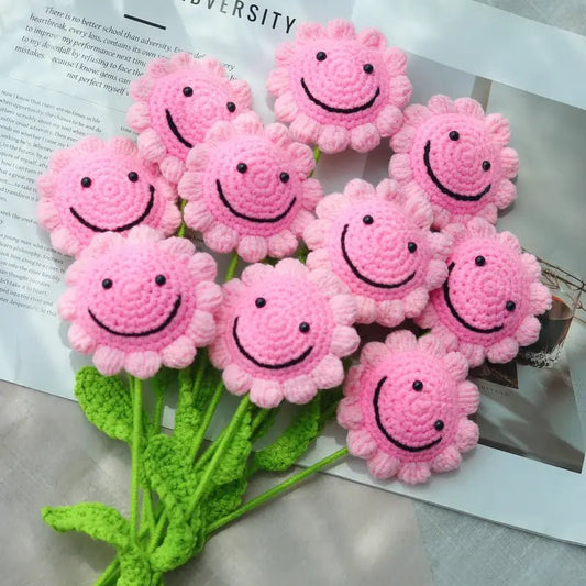 Pink crocheted flower smiley faces with green stems on a textured background