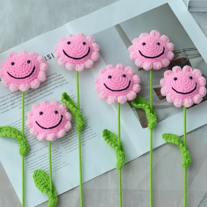 Pink crocheted flower smiley faces with green stems on white background