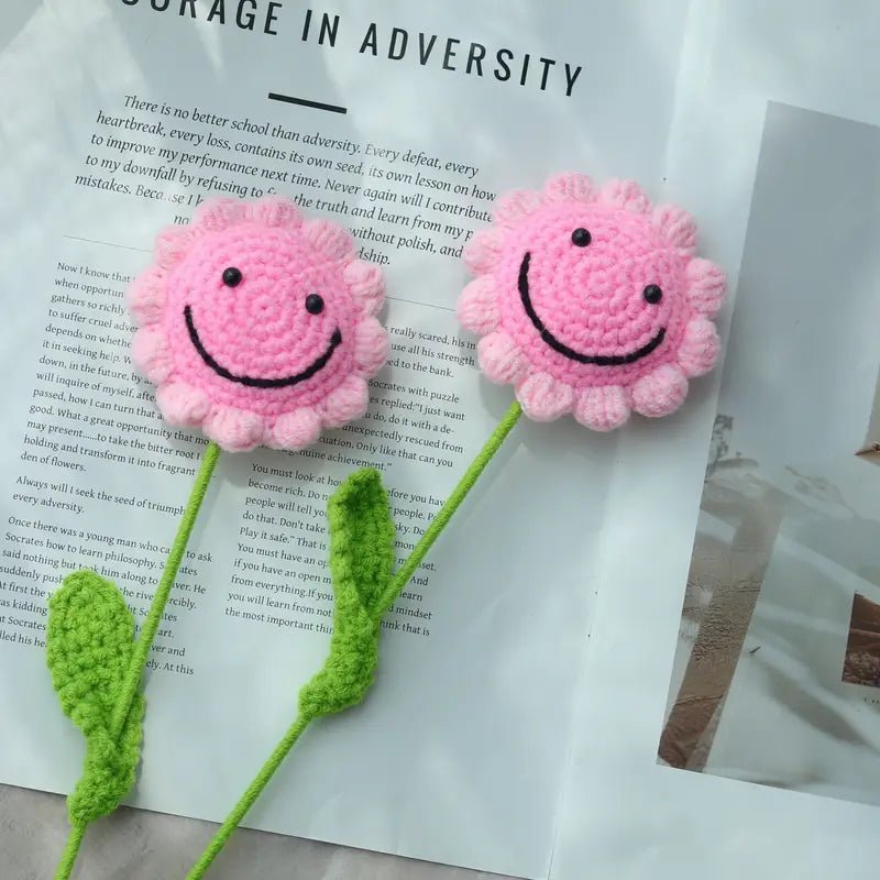 Two pink crocheted flower smiley faces with green stems on a book page