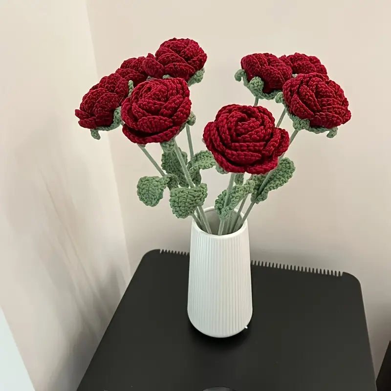 Crocheted red roses with green leaves in a white ribbed vase on a dark surface