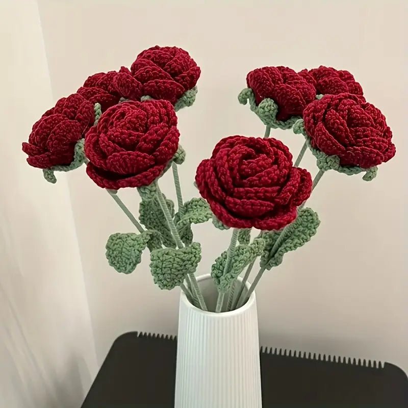 Crocheted red roses with green stems in a white ribbed vase on a black surface