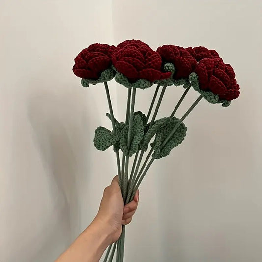 Deep red crocheted roses with green stems held in a hand against a white background