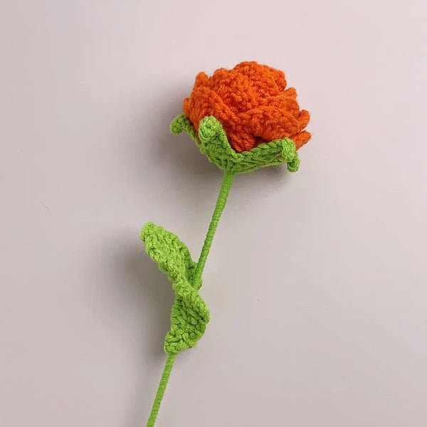 Crocheted orange flower with green stem and leaves against neutral background