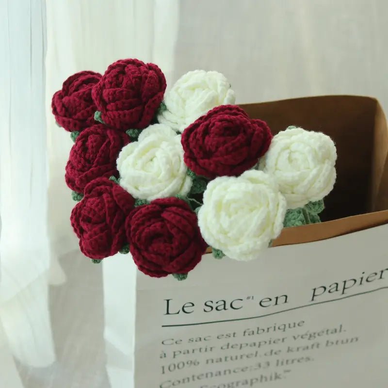 Crocheted red and white roses nestled in a paper bag with French text