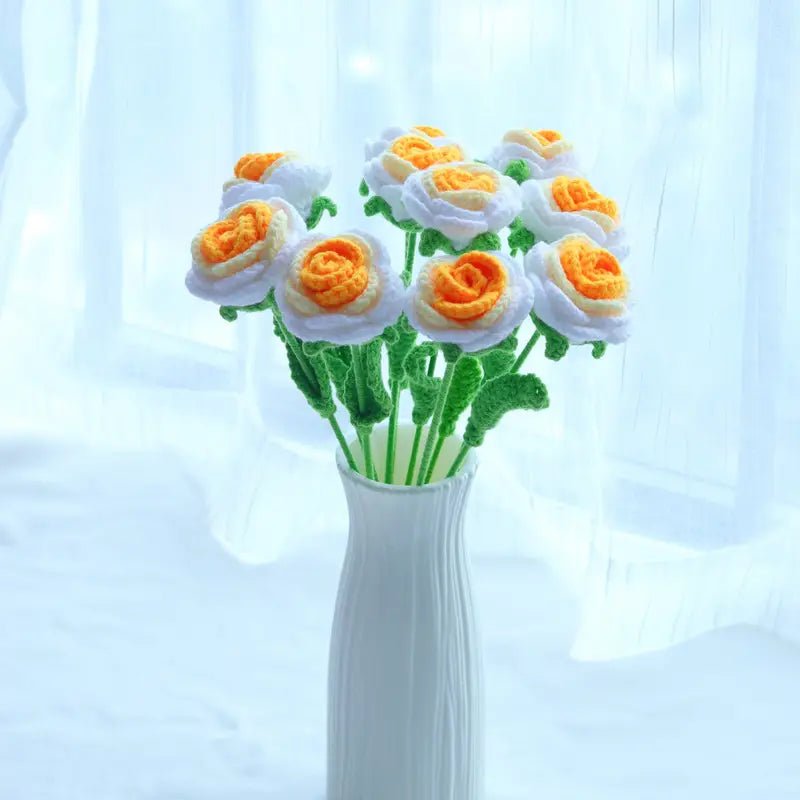 White and orange crocheted flowers with green stems in a tall white vase