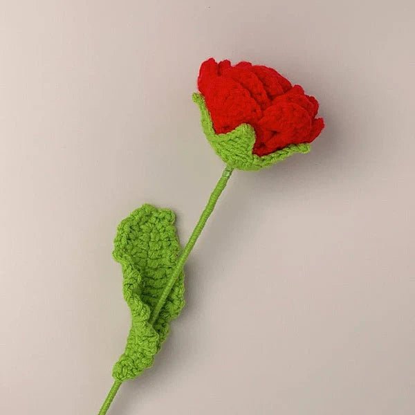 Crocheted red rose with green stem and leaf against neutral background