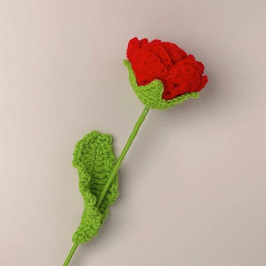 Crocheted red rose with green stem and leaf against neutral background