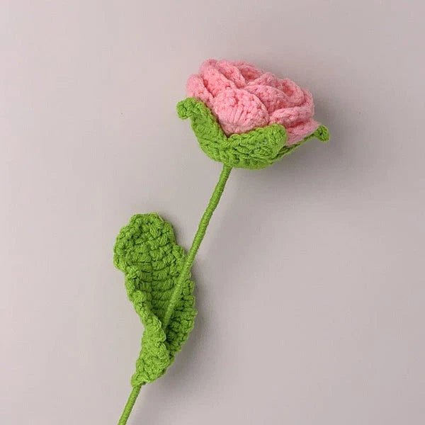 Crocheted pink rose with green stem and leaf on neutral background