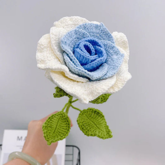 Crocheted rose with blue center and white petals, green leaves and stem