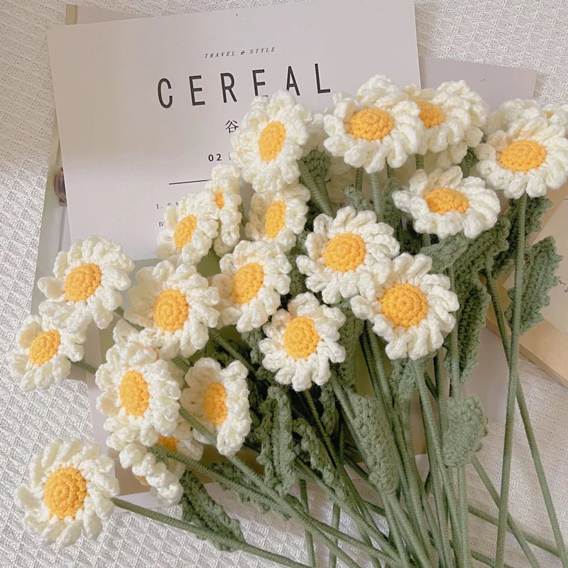 Crocheted white daisies with yellow centers on green stems, resting on a Cereal magazine
