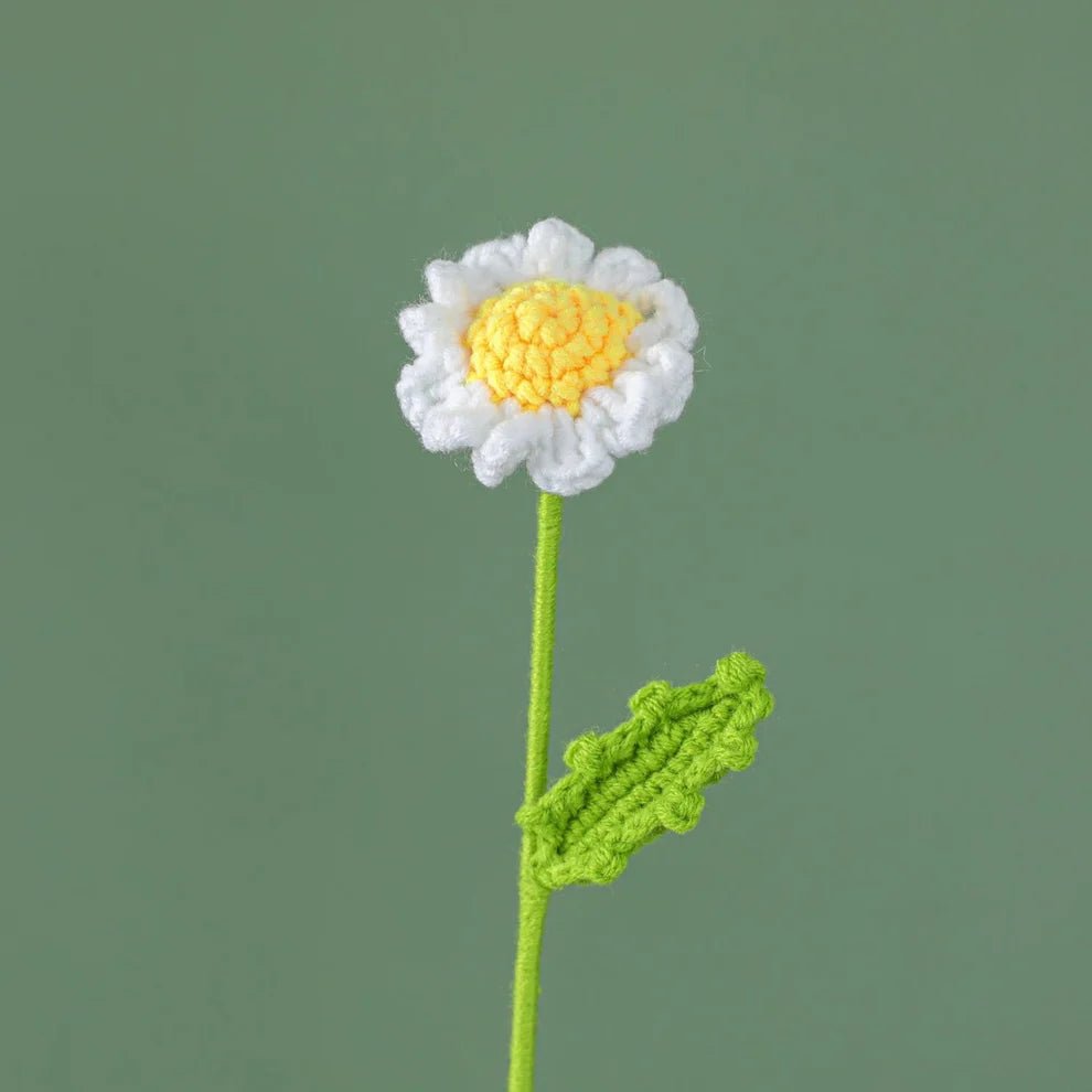 Crocheted white and yellow flower with green stem and leaf against sage background