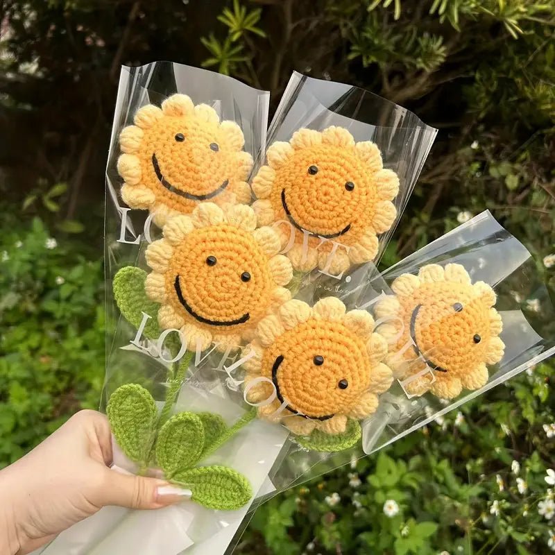 Crocheted yellow smiley sunflowers in clear packaging with green leaves, held by a hand