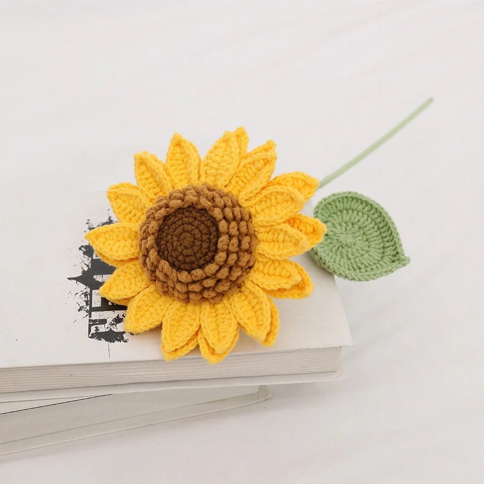 Crocheted yellow sunflower with brown center and green leaf resting on white book
