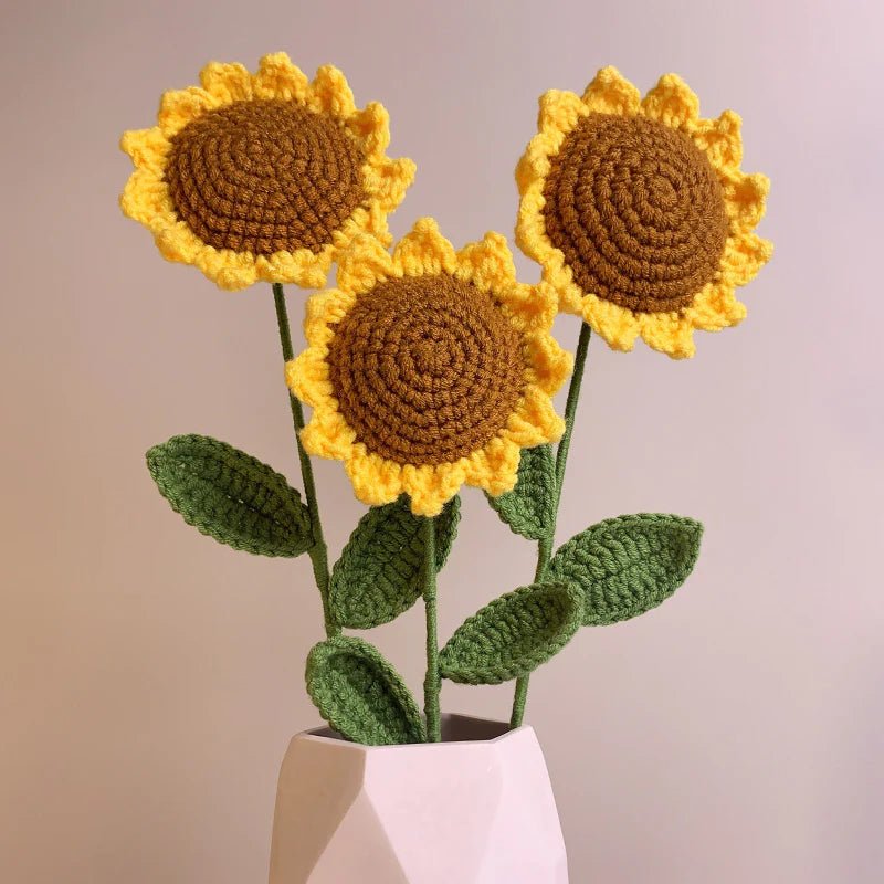 Three crocheted sunflowers with yellow petals and brown centers in a white geometric vase.