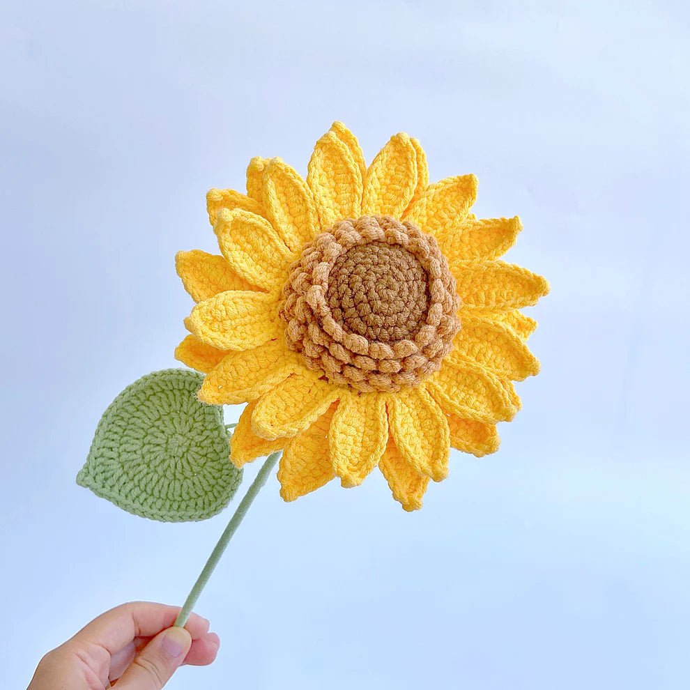 Crocheted yellow sunflower with green leaf against a pale blue background