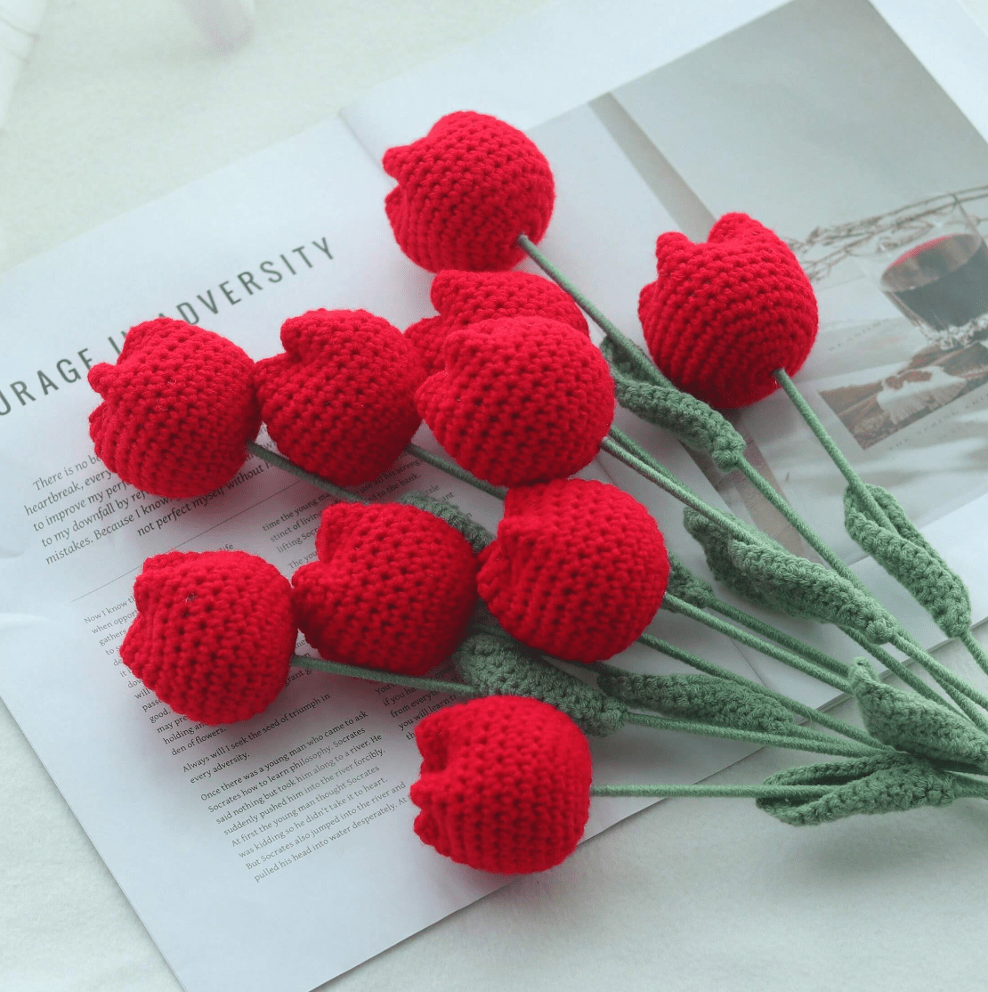 Crocheted red heart flowers with green stems on an open book page