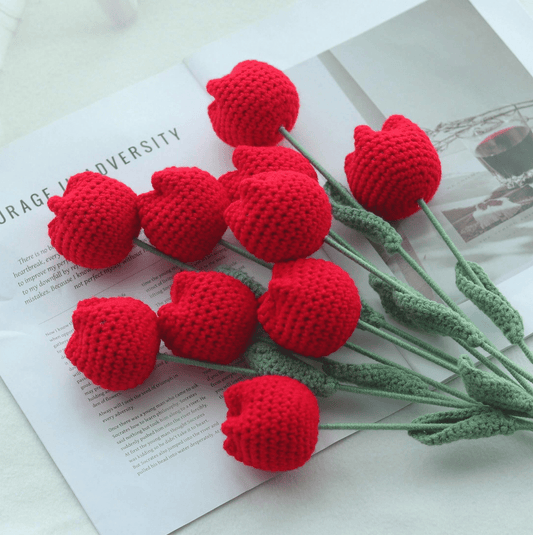 Crocheted red heart flowers with green stems on an open book page