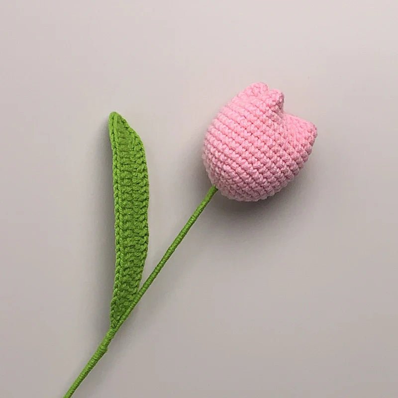 Crocheted pink tulip with green stem against a light gray background