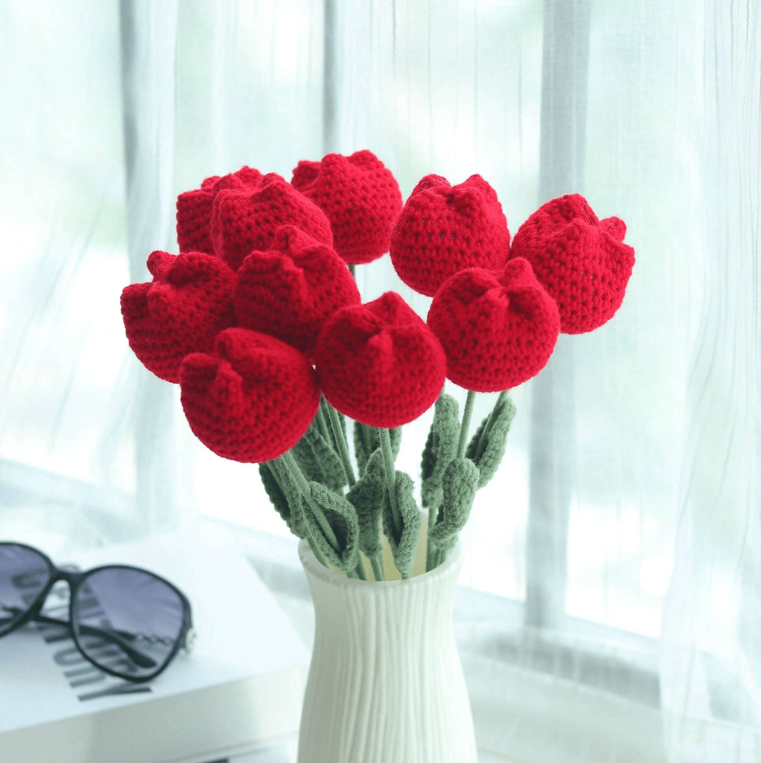 Crocheted red tulips in white vase, with sunglasses on a bright windowsill