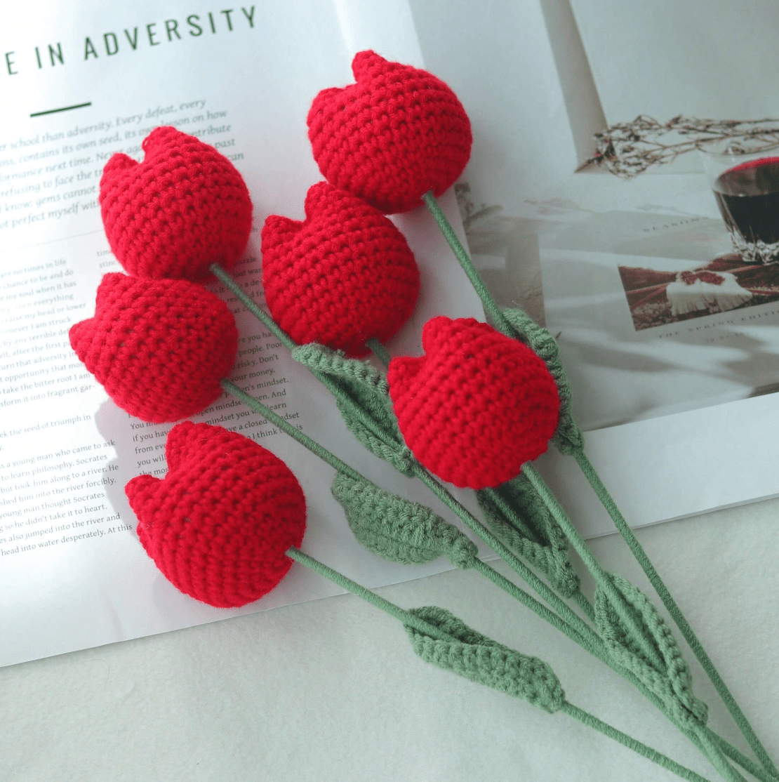 Crocheted red tulips with green stems lying on a book page about adversity