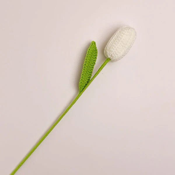 White crocheted tulip with green stem against a neutral background