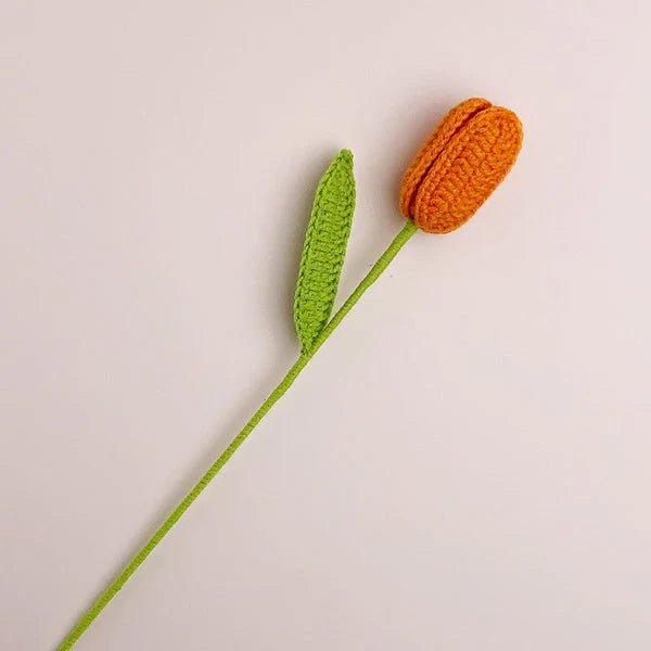 Crocheted orange tulip with green stem against neutral background