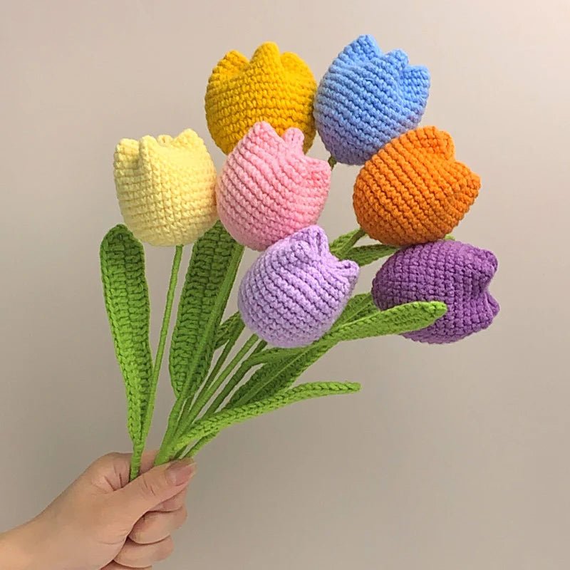 Crocheted tulips in rainbow colors with green stems, held by a hand against a neutral background